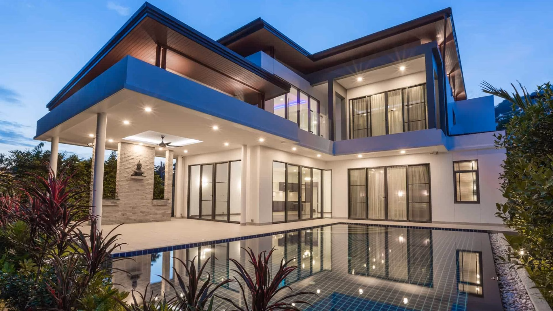 The outside of a luxurious, modern, and contemporary piece of real estate with a large pool and a night sky.