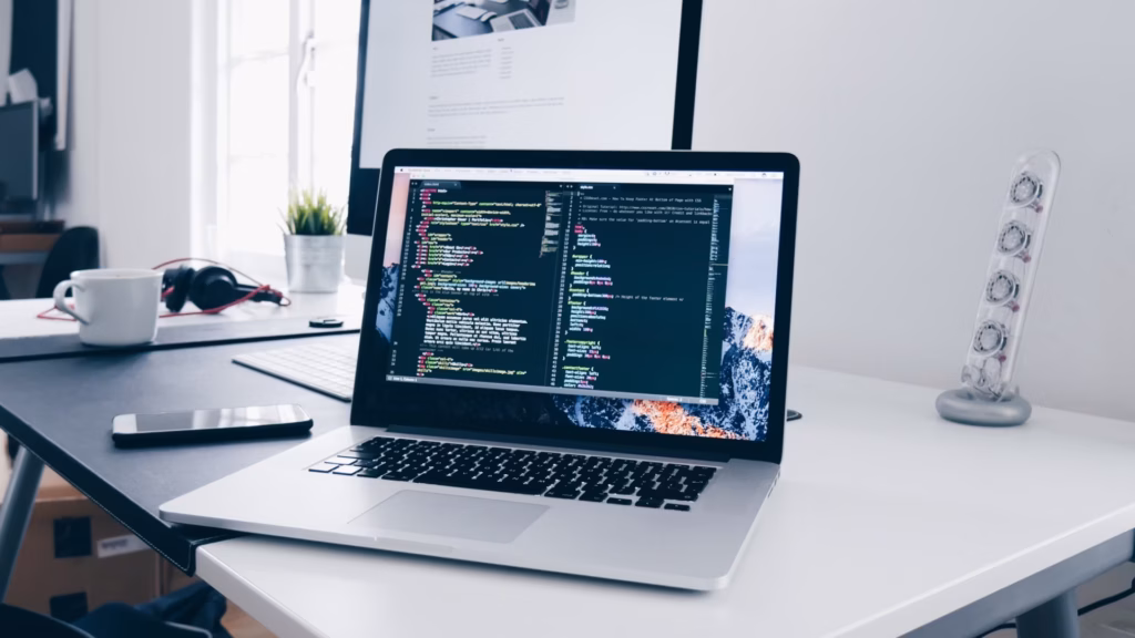A laptop displaying CSS code sites on a white desk, showing the work of a SaaS website builder