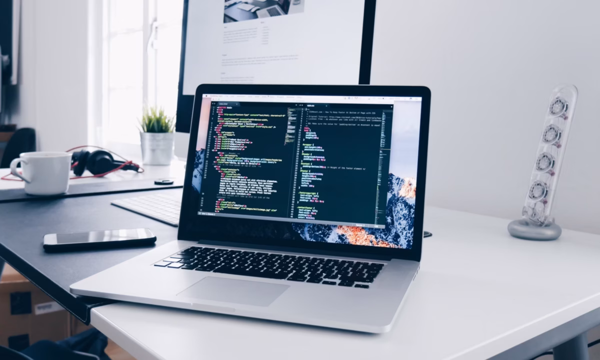 A laptop displaying CSS code sites on a white desk, showing the work of a SaaS website builder