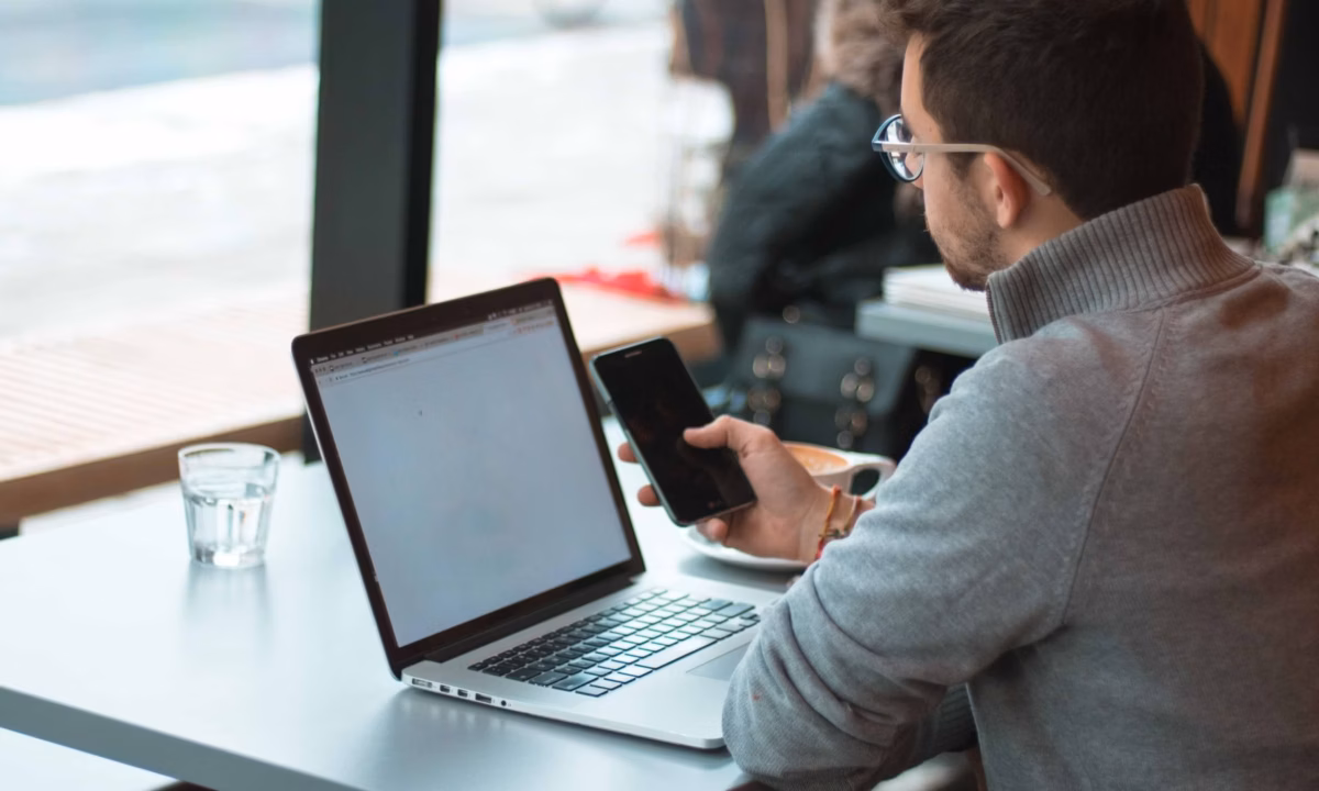 A realtor is in front of his mobile phone and laptop, searching online for best practices for his website and social media strategy.
