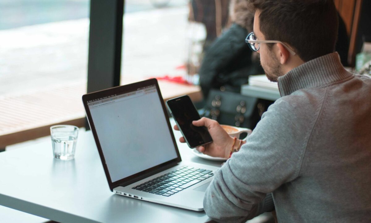 A realtor is in front of his mobile phone and laptop, searching online for best practices for his website and social media strategy.