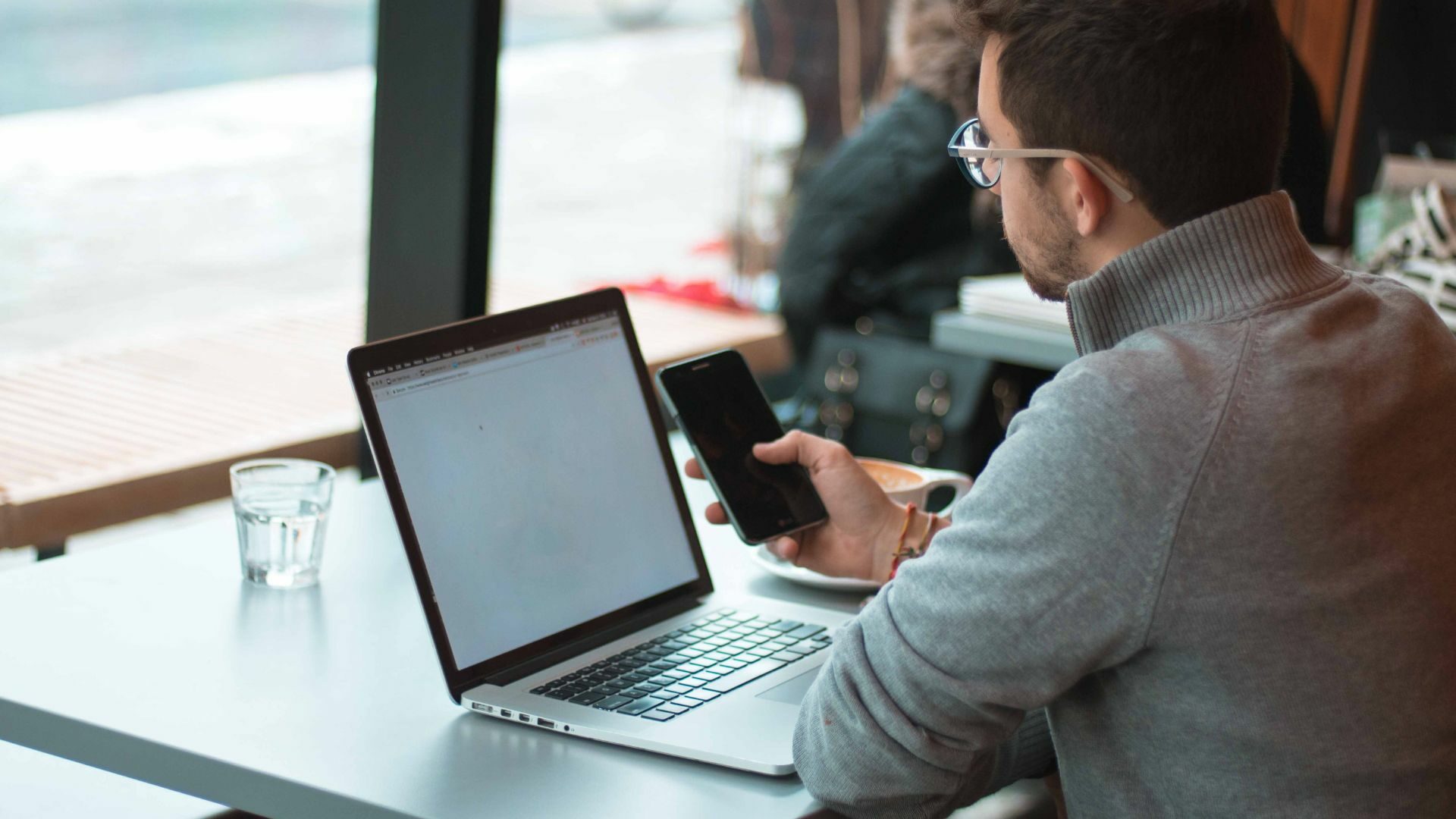 A realtor is in front of his mobile phone and laptop, searching online for best practices for his website and social media strategy.