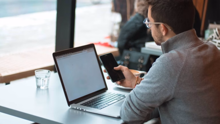 A realtor is in front of his mobile phone and laptop, searching online for best practices for his website and social media strategy.