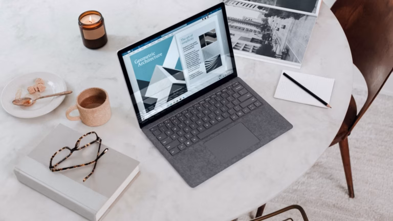 A laptop, notebook, glasses, notepad, pen, coffee, and candle are on top of a table.