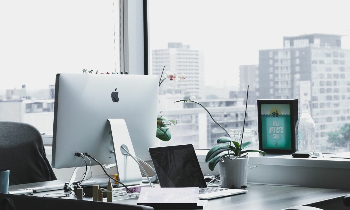 A workspace with a Mac, plants, and city buildings in the background.