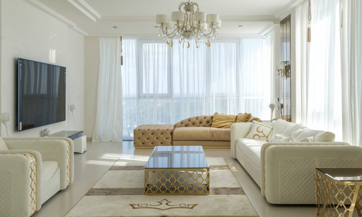 Interior design of a luxurious, clean, white, gold, and modern living room with a large, flat television.