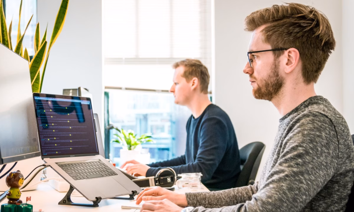 Two people sitting in front of computers in an open office, working on virtual staging projects for real estate agents