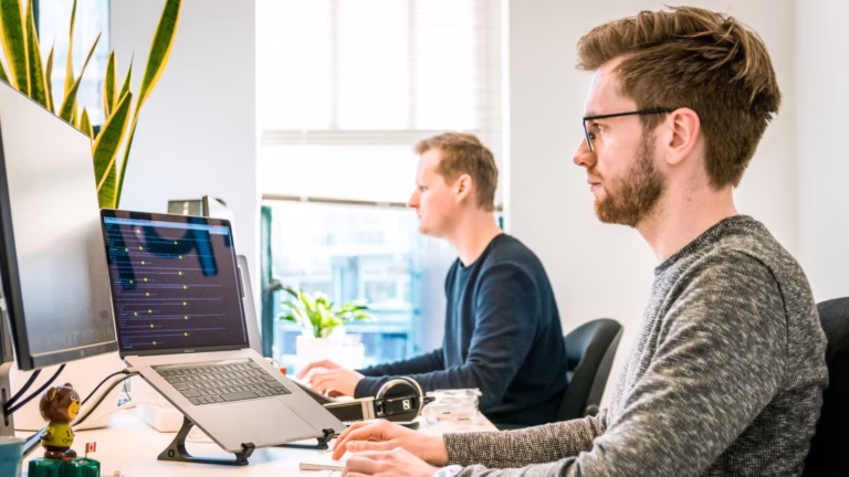 Two people sitting in front of computers in an open office, working on virtual staging projects for real estate agents