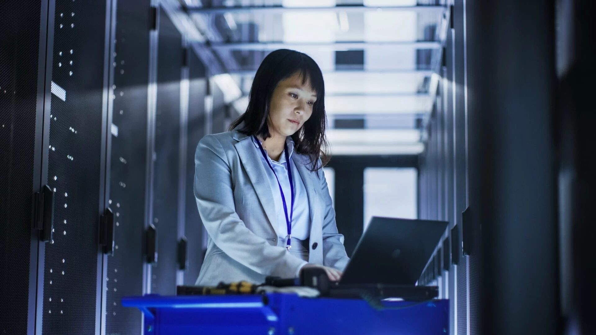 An IT professional works in front of her laptop inside a server room.