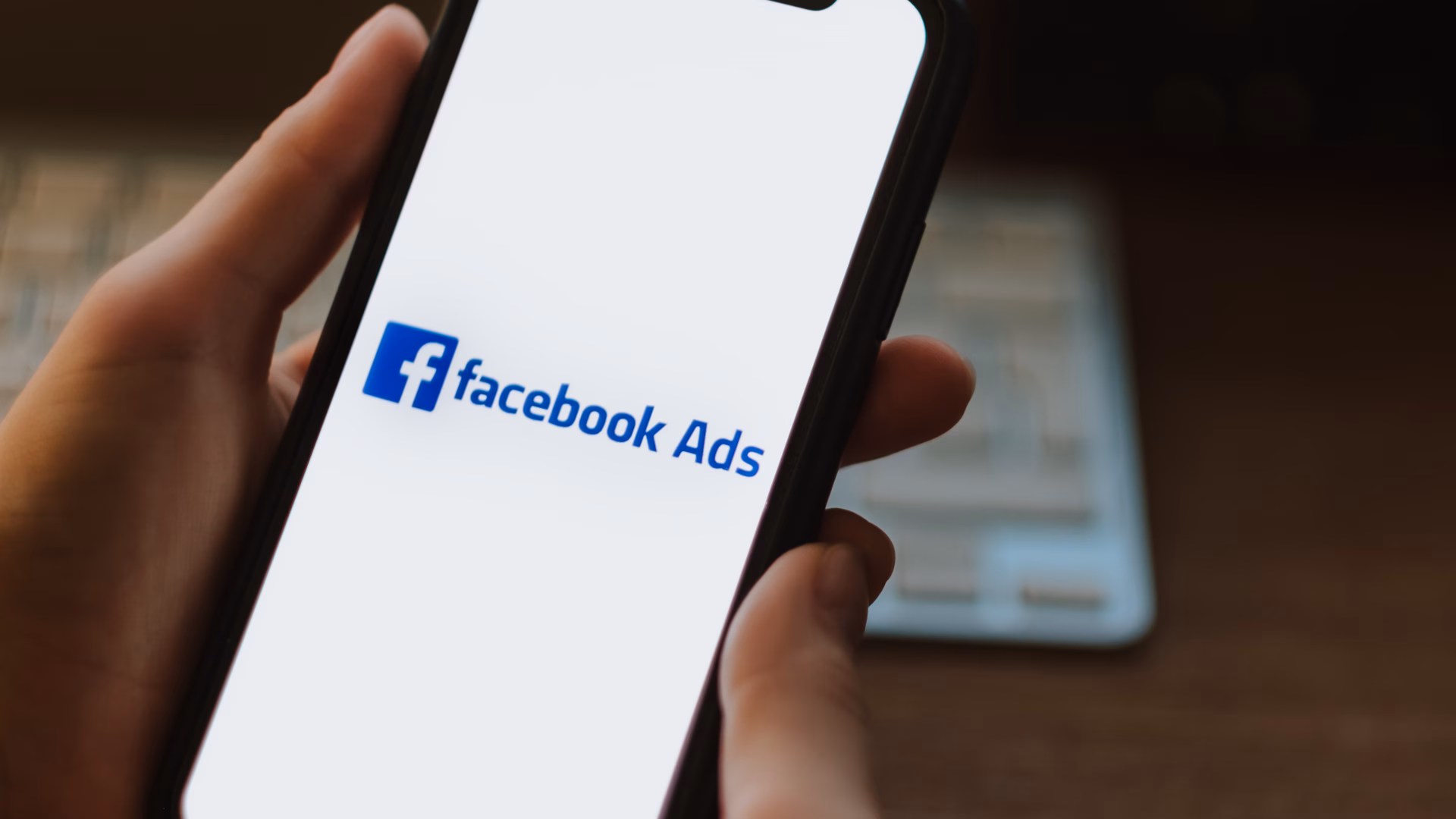 A real estate agent holds a smartphone with a Facebook ads logo.