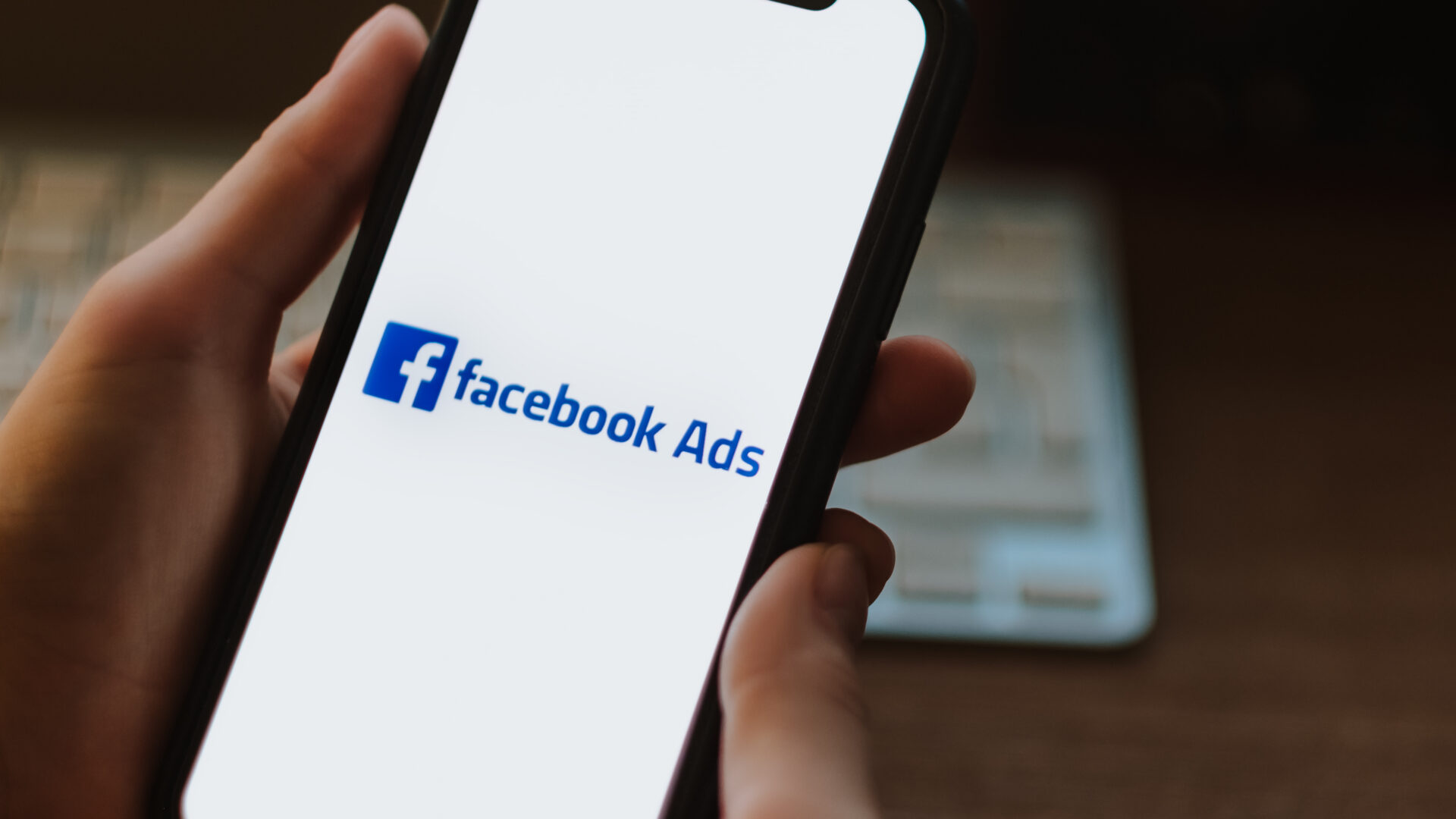 A real estate agent holds a smartphone with a Facebook ads logo.