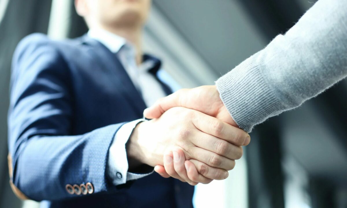 A real estate agent in a business suit shakes hands with a new client.