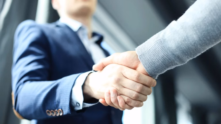 A real estate agent in a business suit shakes hands with a new client.