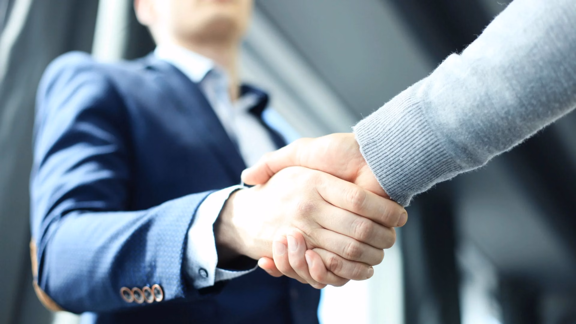 A real estate agent in a business suit shakes hands with a new client.