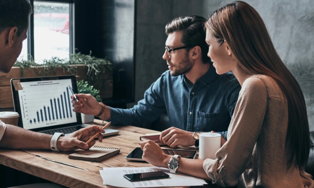 A group of real estate agents discuss the metrics of their marketing efforts inside a meeting room.