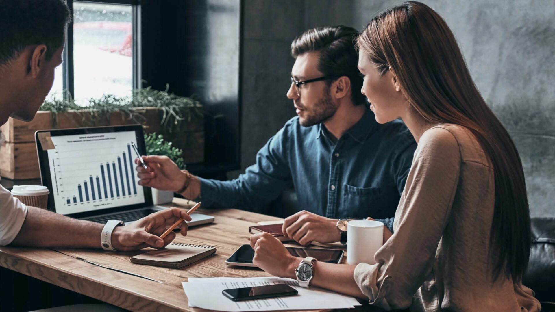 A group of real estate agents discuss the metrics of their marketing efforts inside a meeting room.