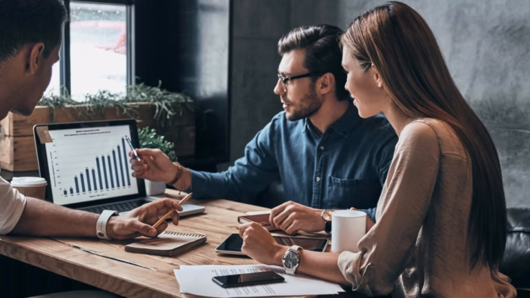A group of real estate agents discuss the metrics of their marketing efforts inside a meeting room.