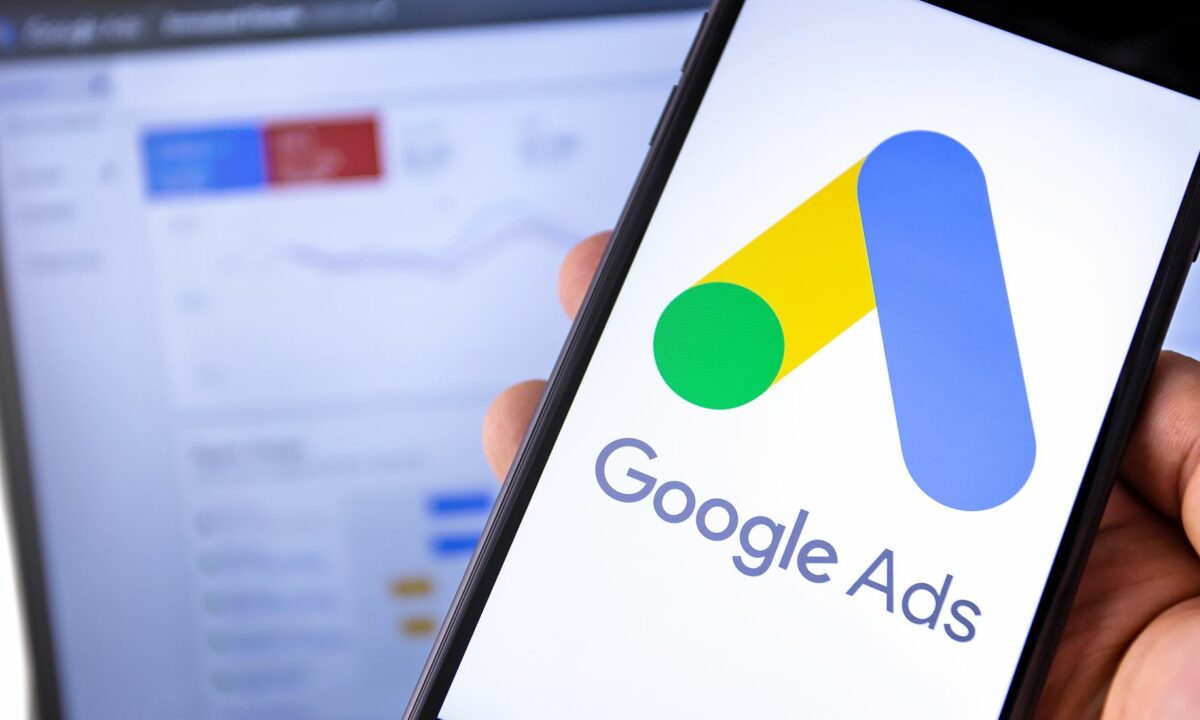 A mobile phone with the Google Ads account logo and a laptop in the background with the Google Ads dashboard for the real estate agent's real estate website.