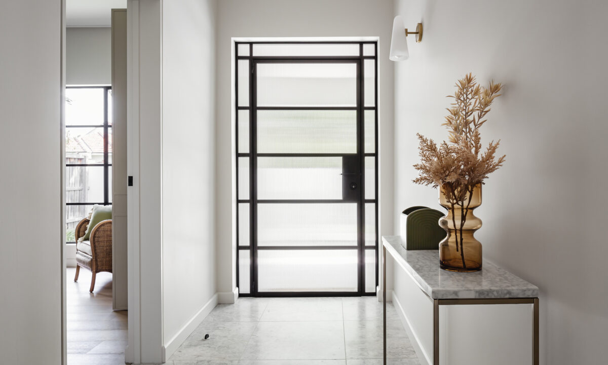 Entry hall of a renovated house with fluted glass steel front door, marble floor tiles and brass console table