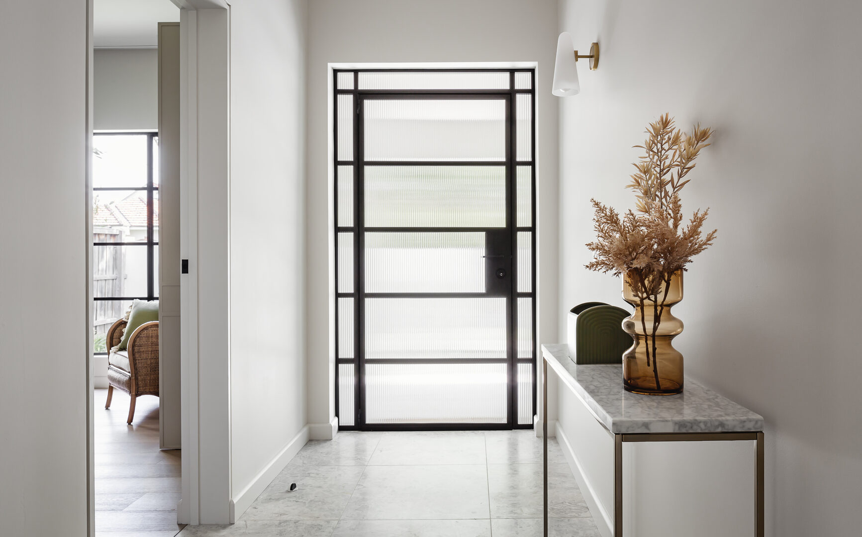 Entry hall of a renovated house with fluted glass steel front door, marble floor tiles and brass console table