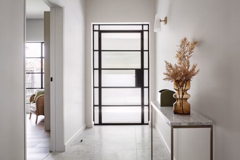 Entry hall of a renovated house with fluted glass steel front door, marble floor tiles and brass console table