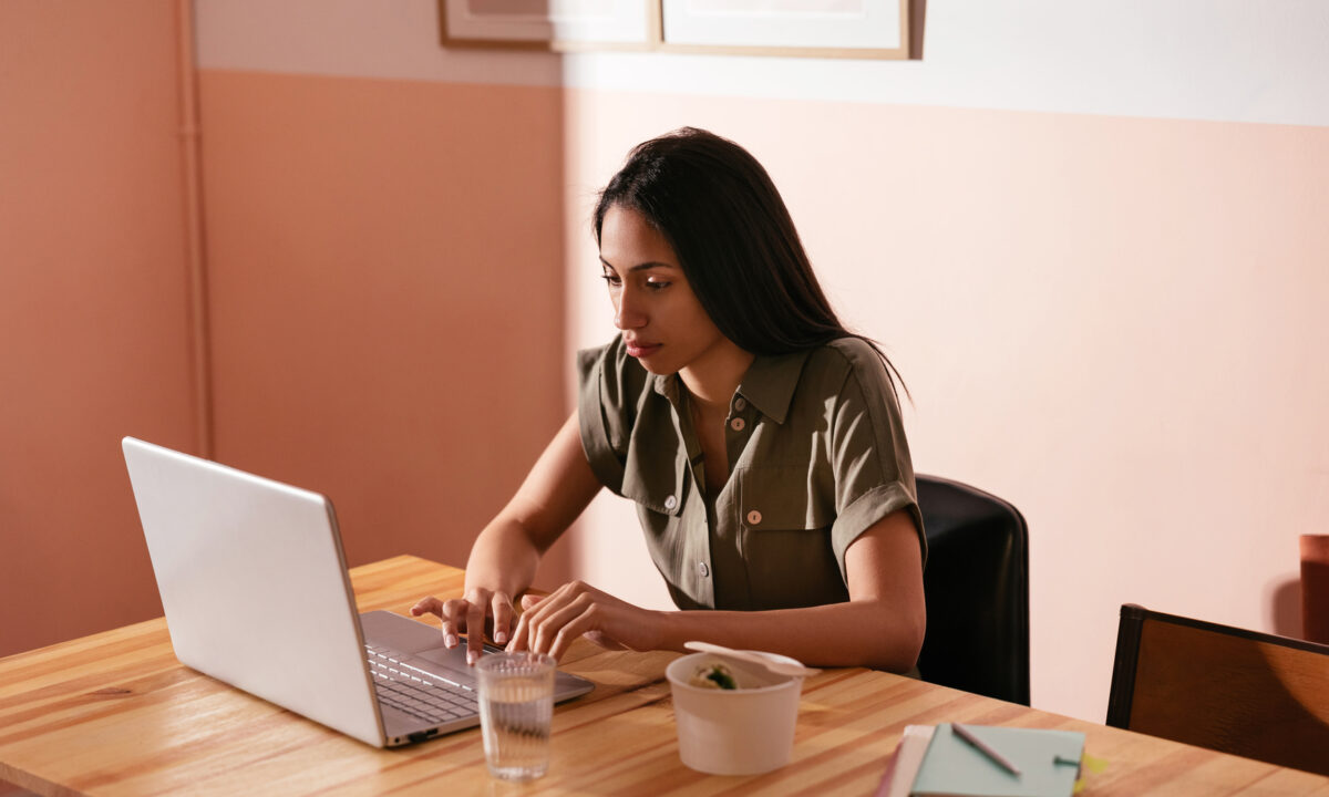 Focused female freelancer browsing netbook and on remote project while sitting at table with takeaway food and glass of water