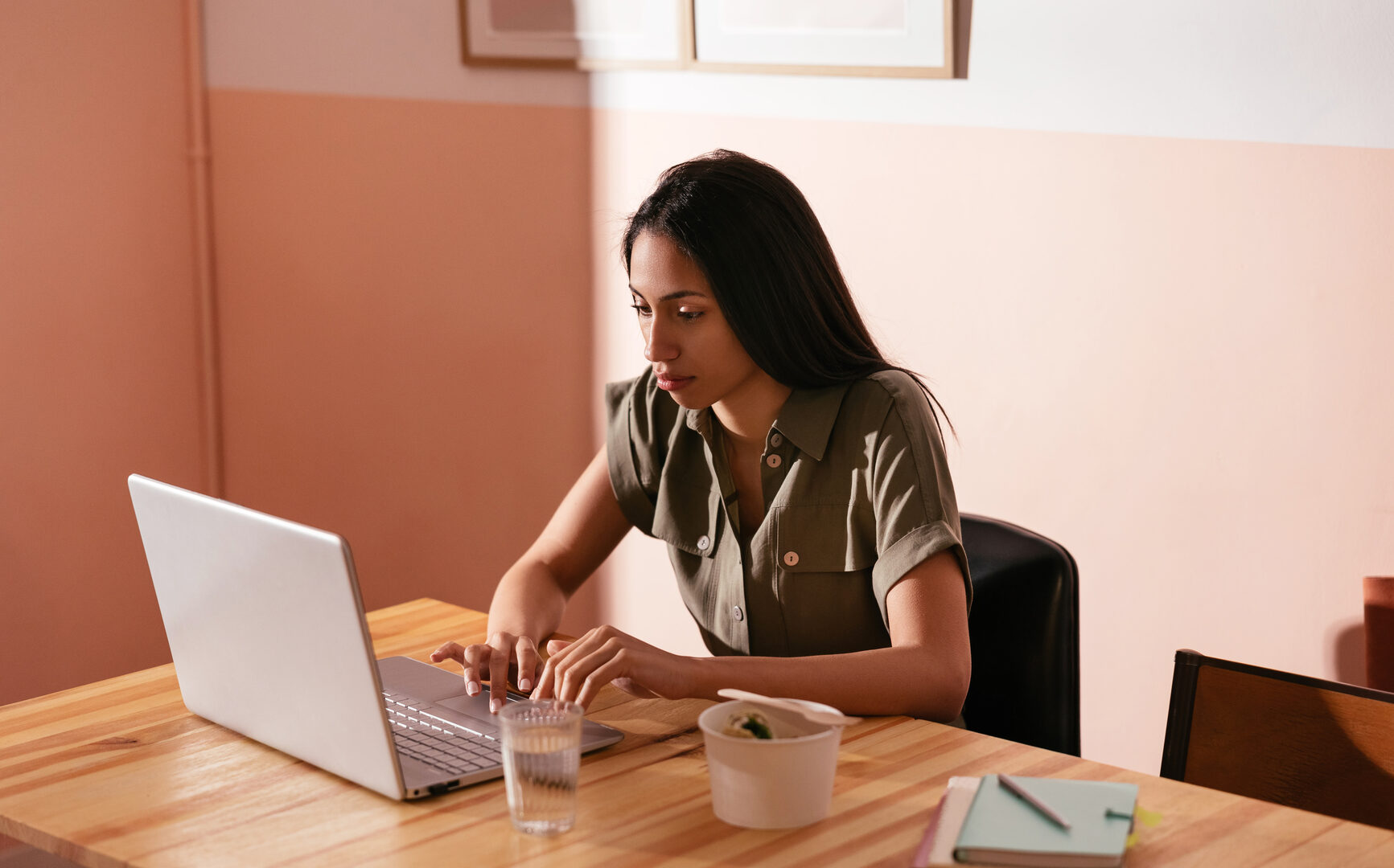 Focused female freelancer browsing netbook and on remote project while sitting at table with takeaway food and glass of water