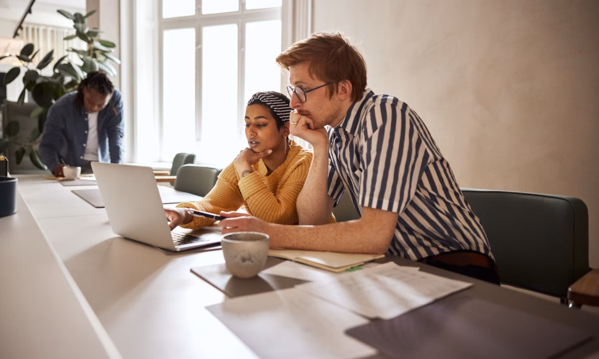 Two young businesspeople working together on a laptop while sitting at a desk in a modern office