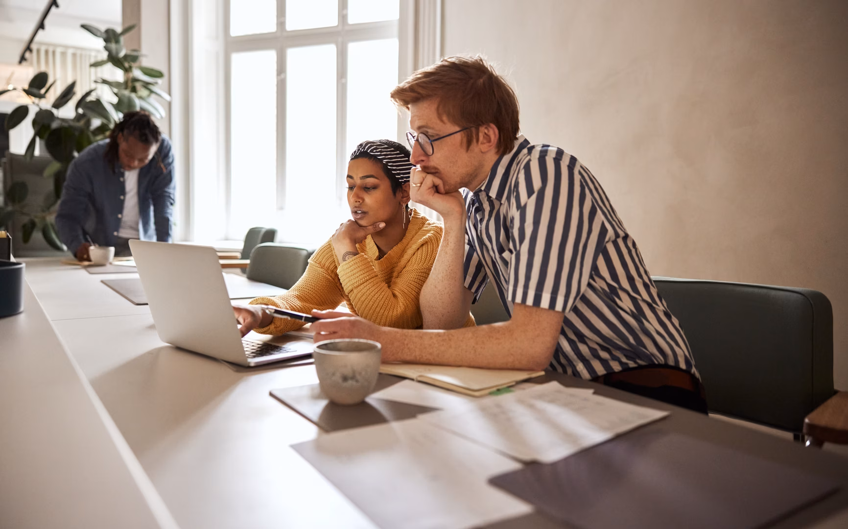 Two young businesspeople working together on a laptop while sitting at a desk in a modern office