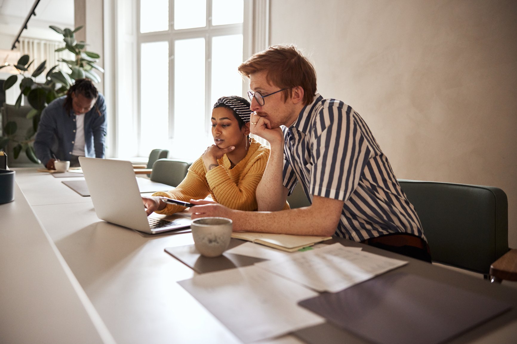 Two young businesspeople working together on a laptop while sitting at a desk in a modern office