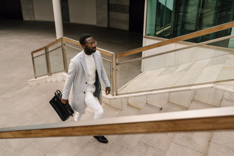 From above of serious African American male entrepreneur in elegant outfit with briefcase walking upstairs of modern business center in city