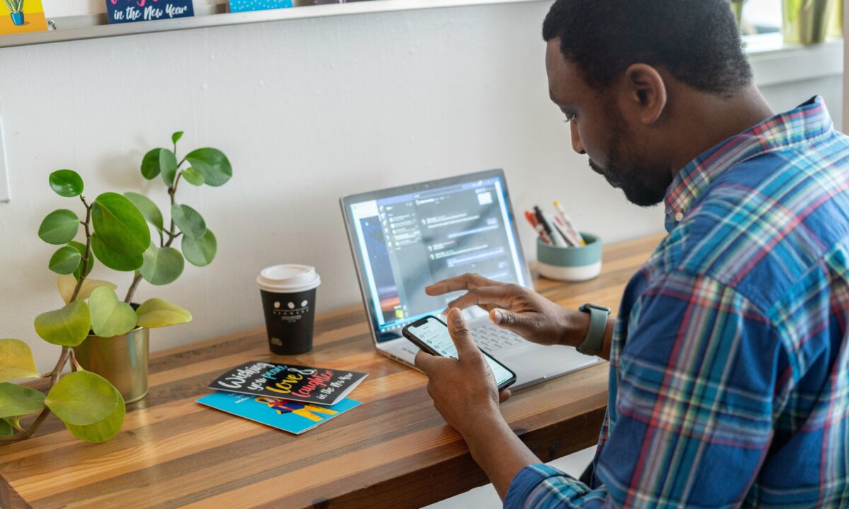 A real estate agent is working using his phone and a laptop computer to maximize the efficiency of his sales funnel.