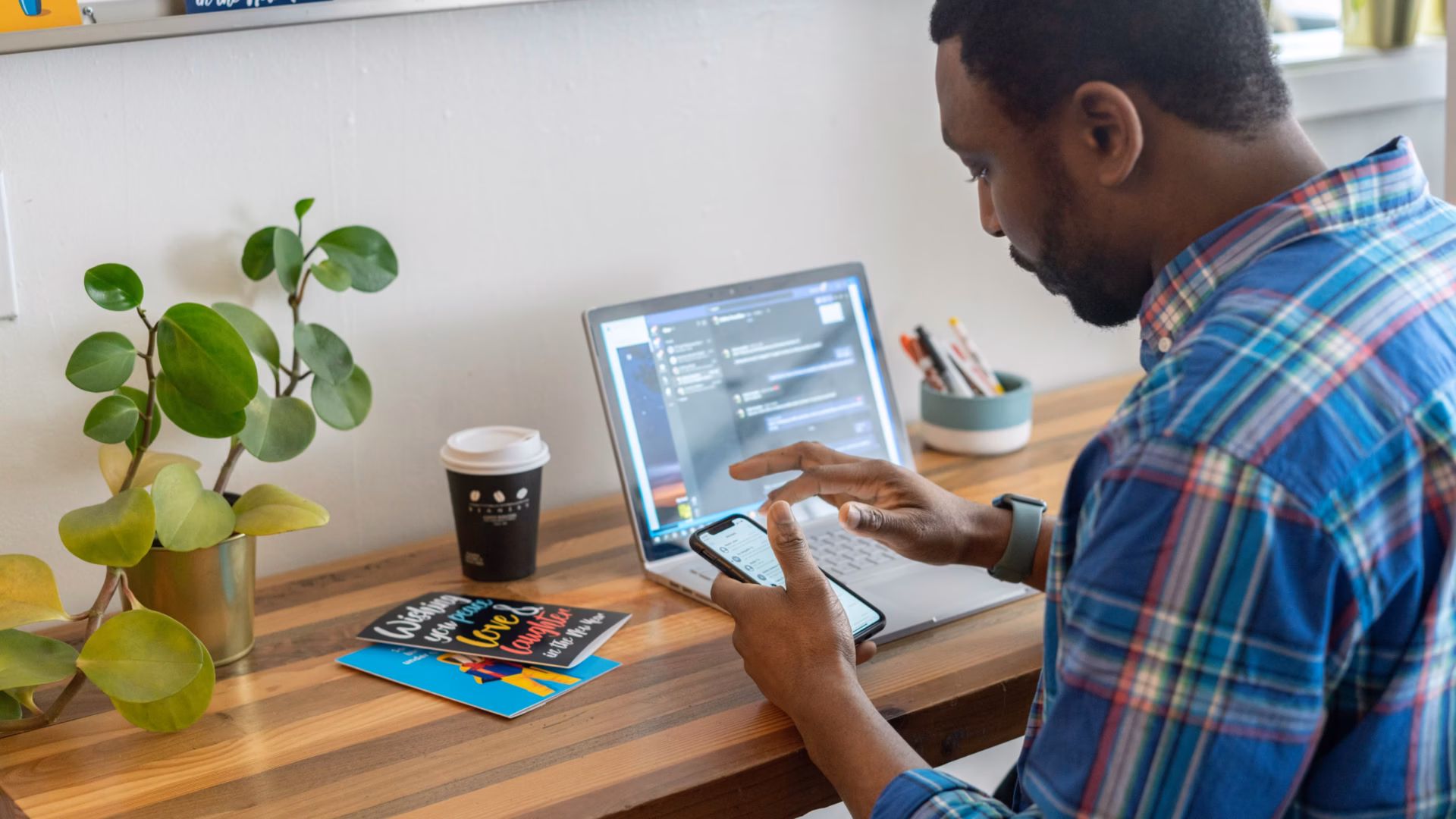 A real estate agent is working using his phone and a laptop computer to maximize the efficiency of his sales funnel.