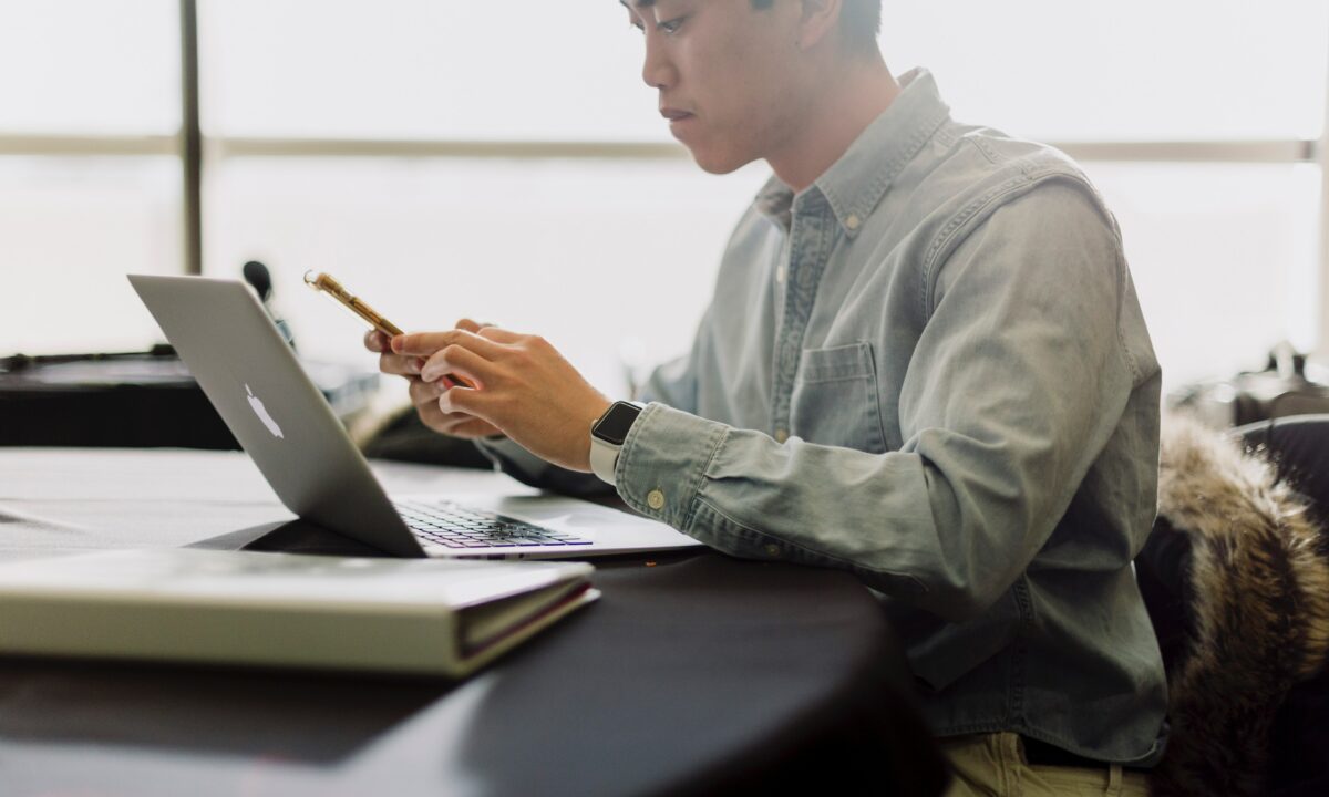 A real estate agent using a phone and a laptop, searches for pricing information for an IDX website online.