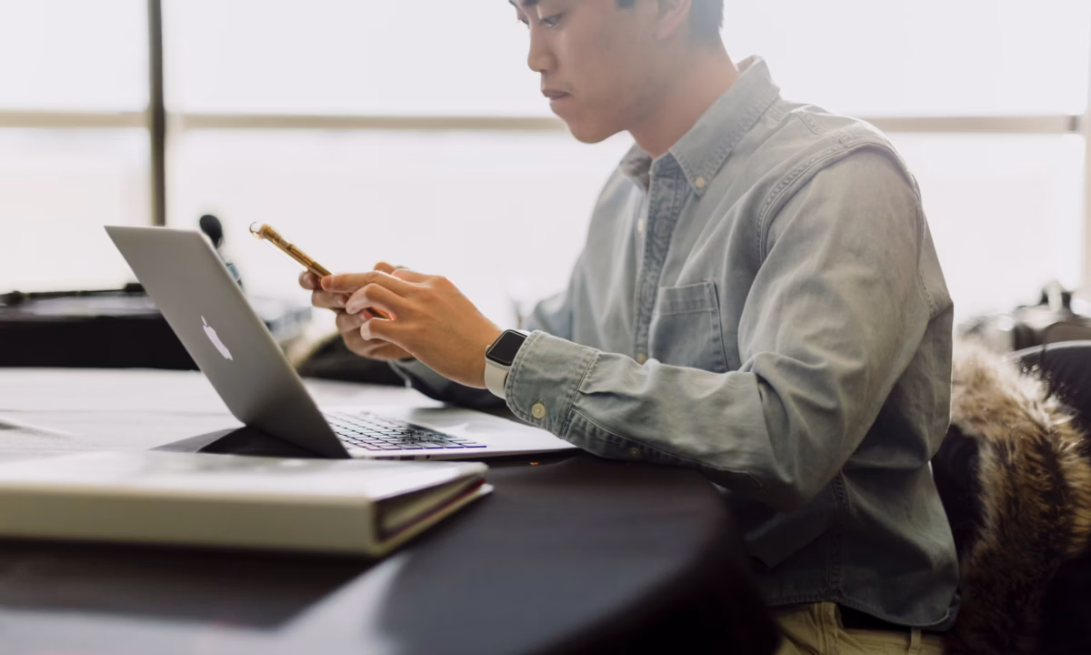 A real estate agent using a phone and a laptop, searches for pricing information about IDX website cost online.