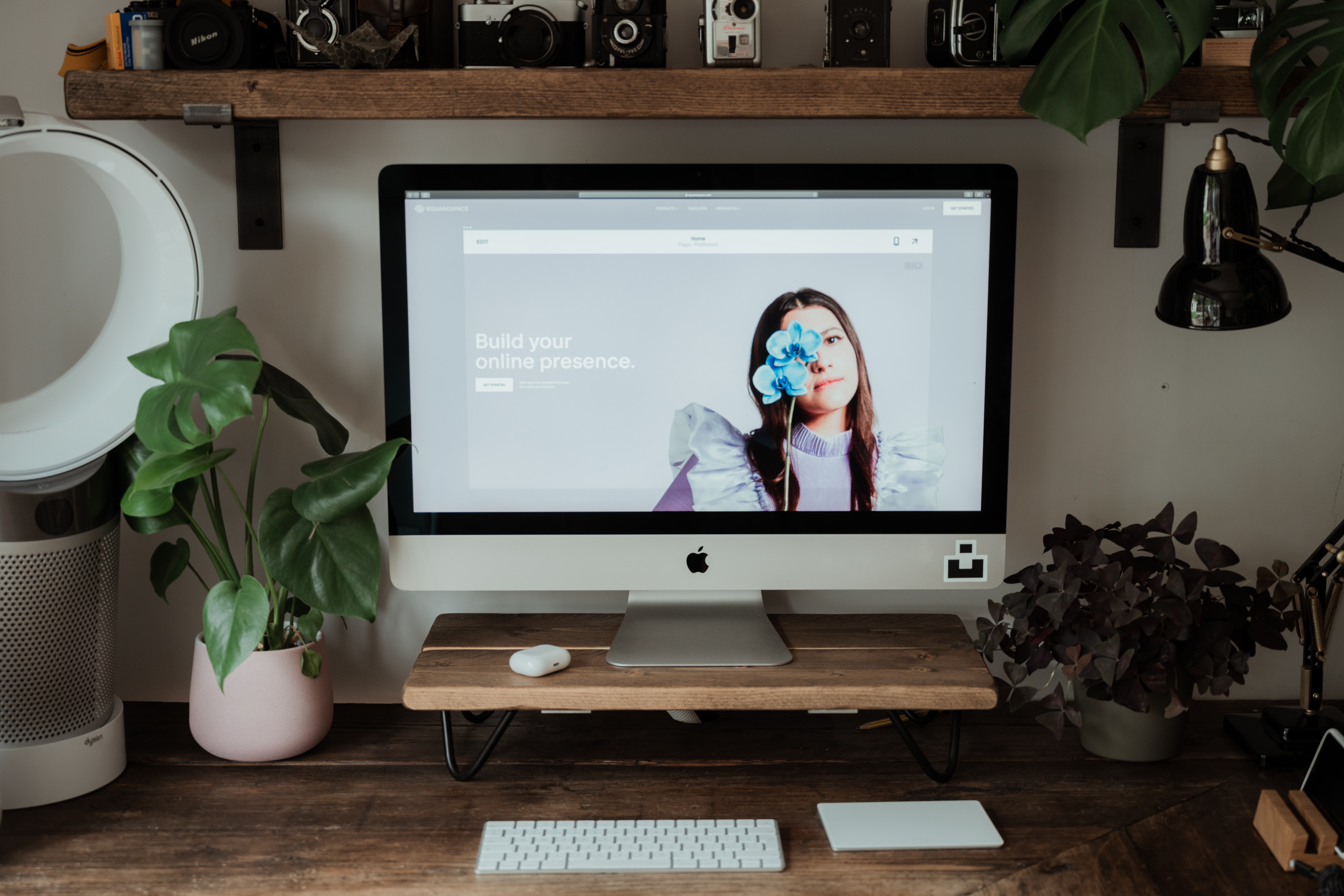 A Squarespace real estate website preview is displayed on a desktop computer atop a clean and minimalist workstation.