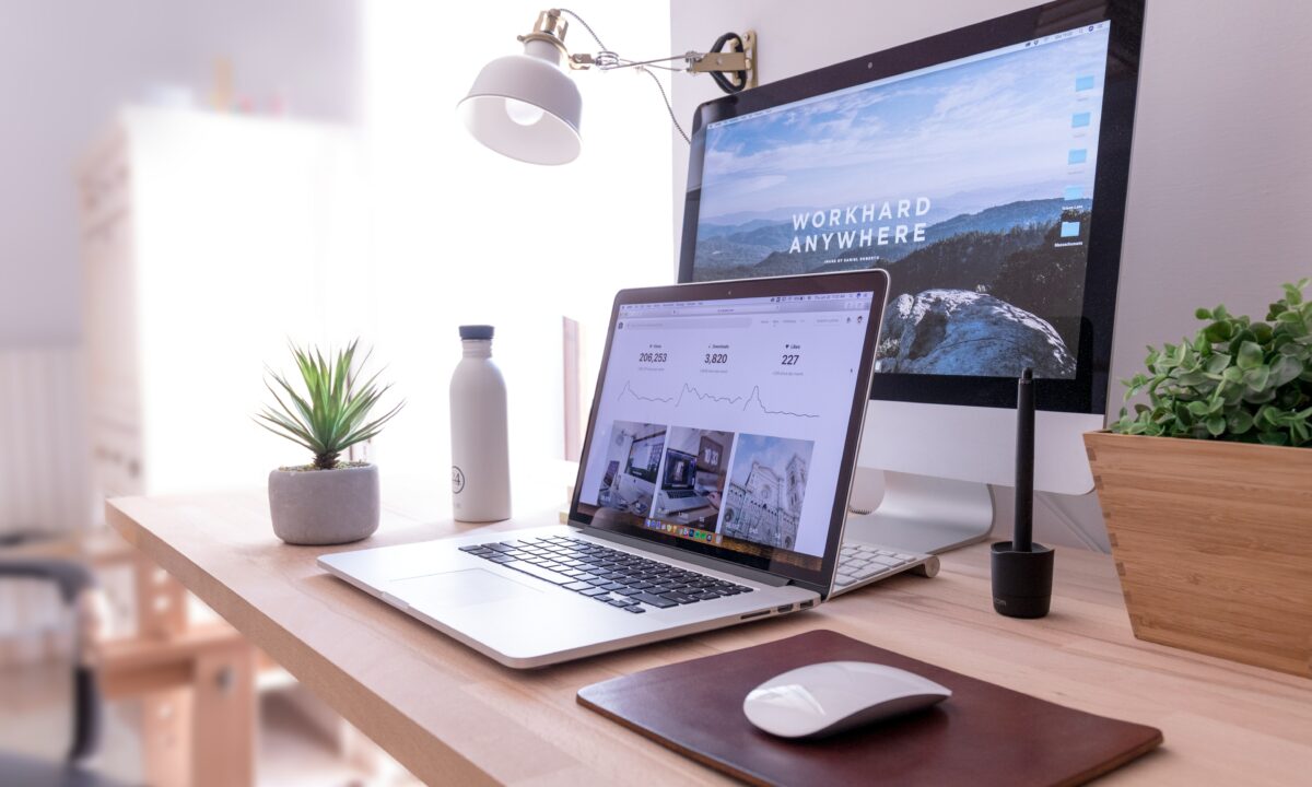 A laptop and desktop computer display a real estate website builder preview on a clean and minimalist workstation.