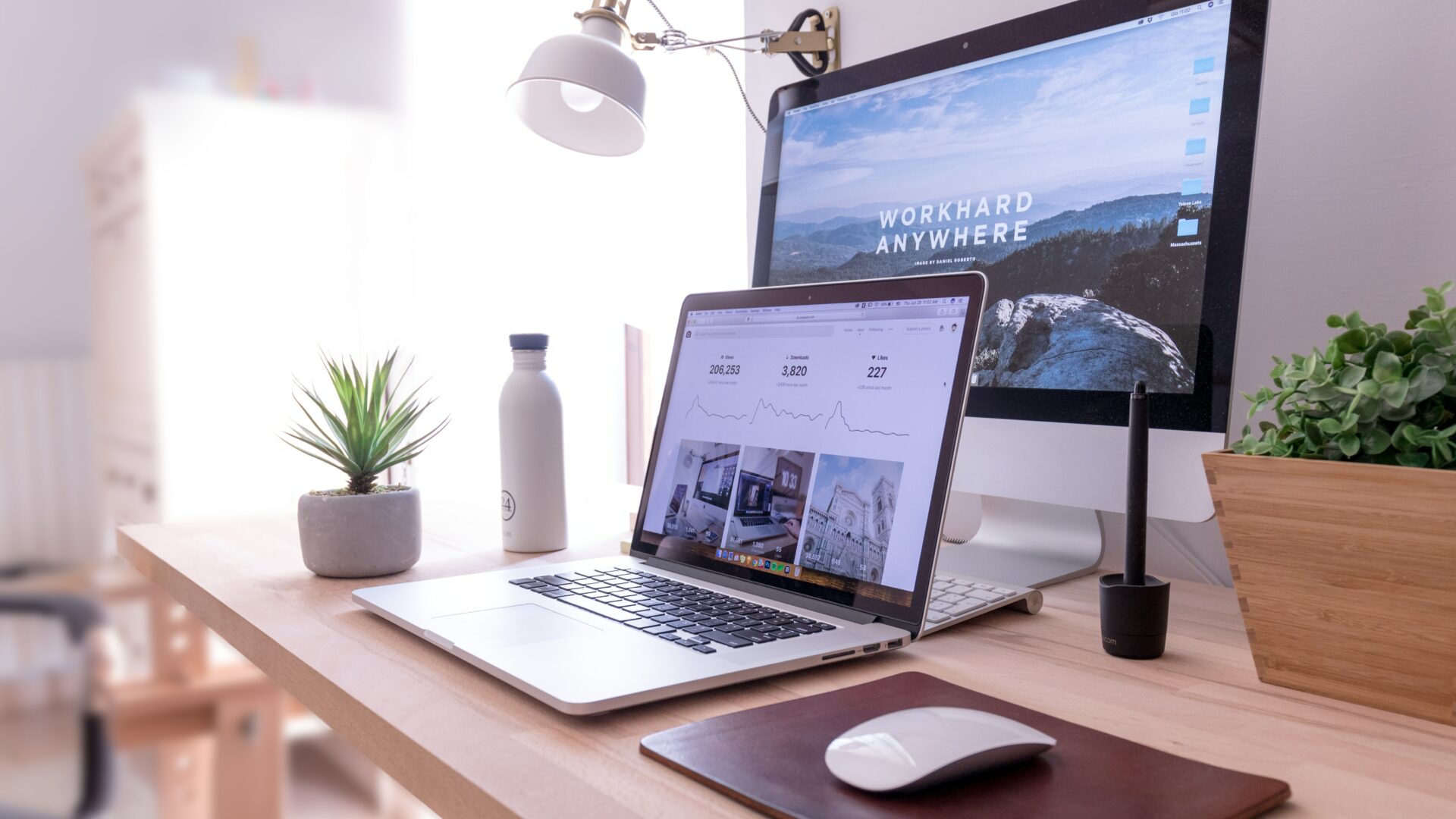 A laptop and desktop computer display a real estate website builder preview on a clean and minimalist workstation.