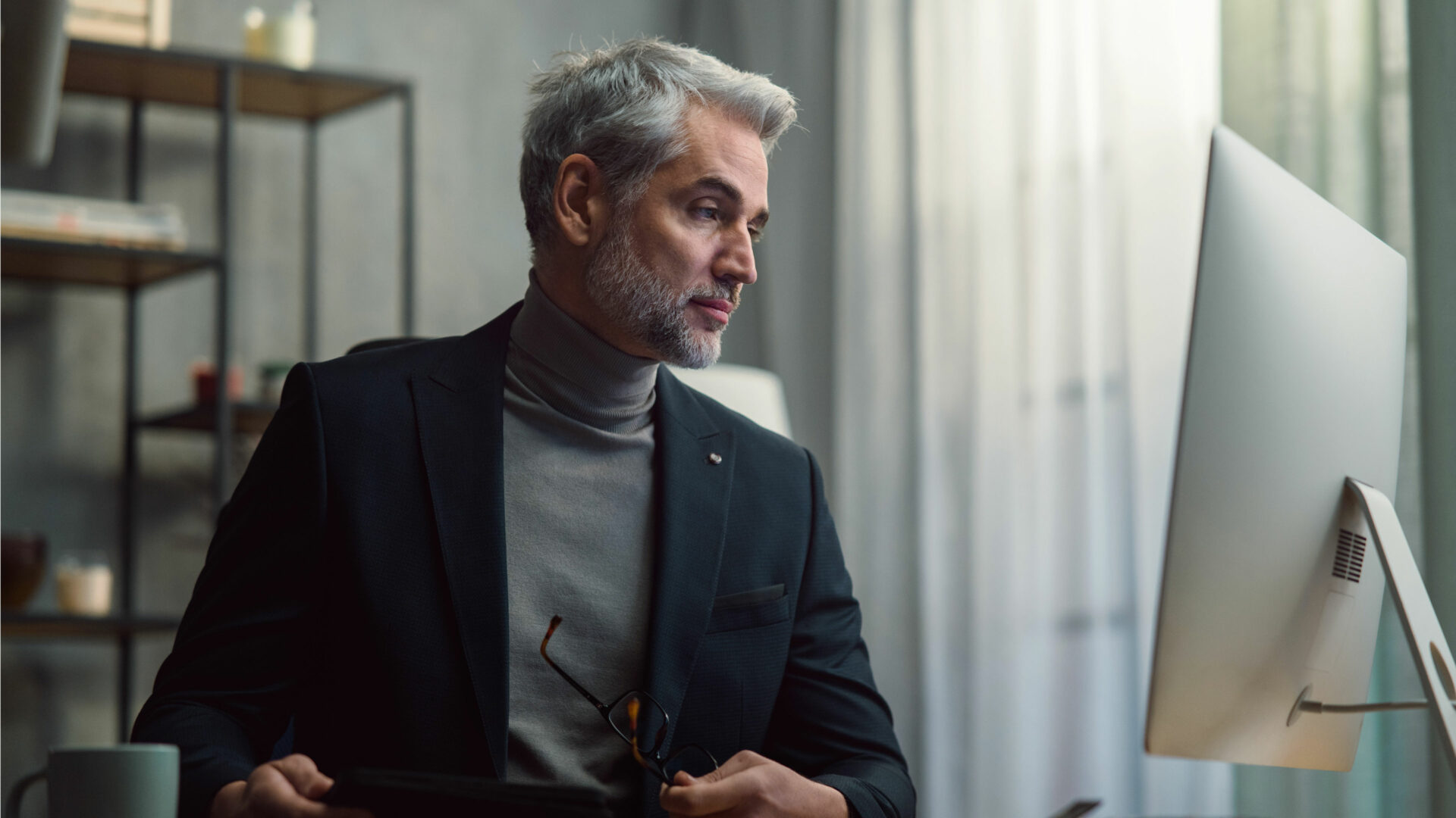 Older male real estate agent sitting at desk looking at the computer screen and auditing his current branding to attract more business.