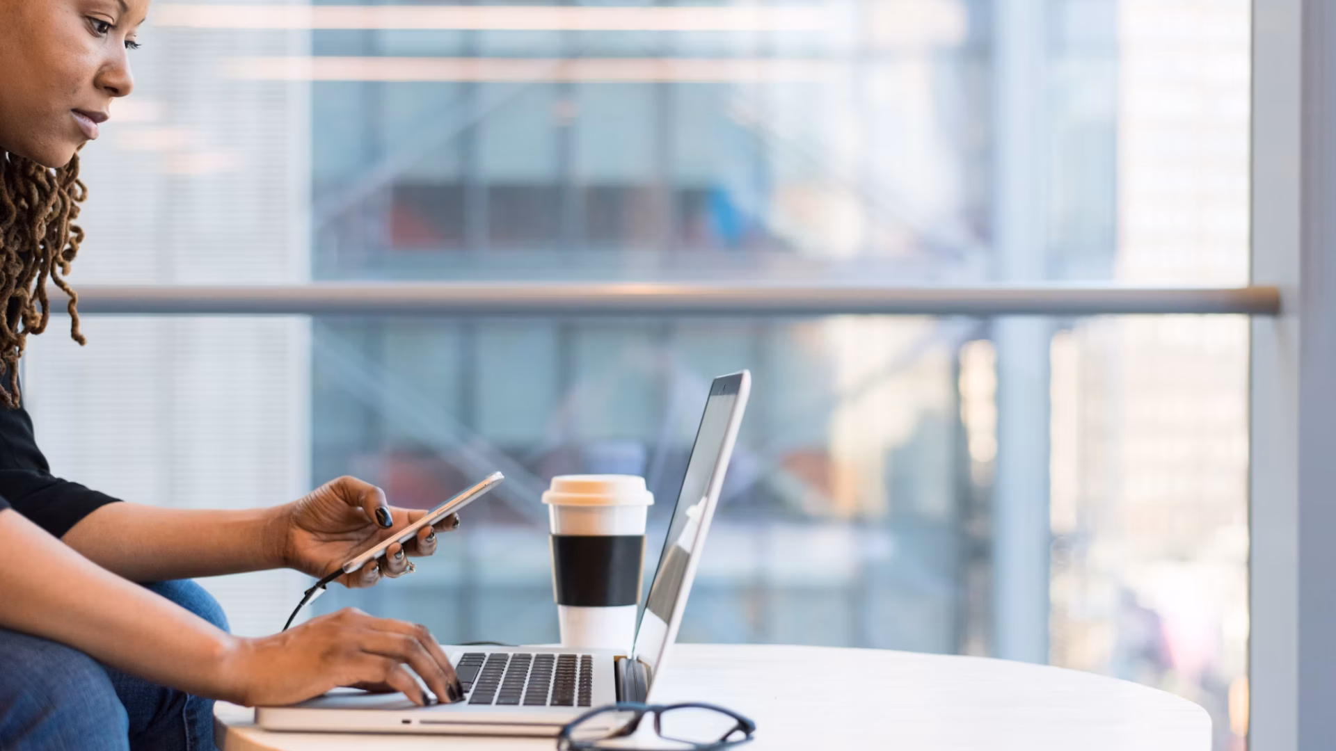 woman holding smartphone and navigating on a computer on a coffee table, demonstrating the work of an ISA real estate strategist