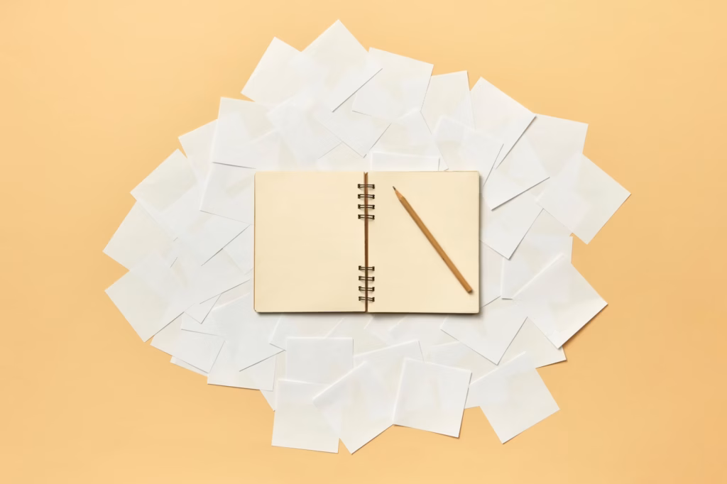 A pencil sits on top of a blank book where an agent is coming up with real estate words and creative real estate listing descriptions examples for their marketing