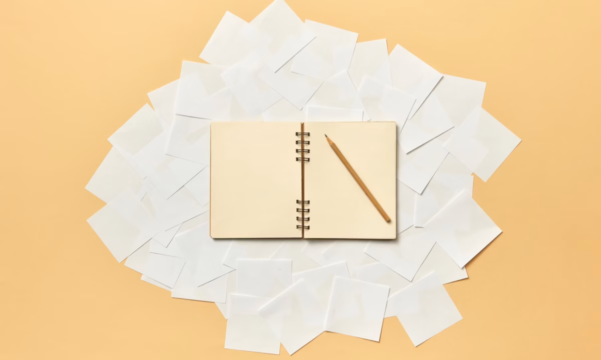 A pencil sits on top of a blank book where an agent is coming up with real estate words and creative real estate listing descriptions examples for their marketing