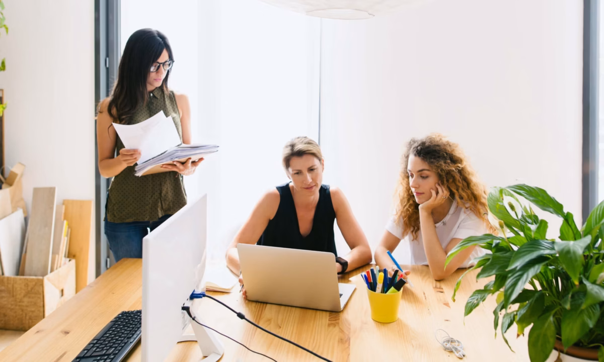 Three business people gather around a table with a laptop and paperwork, demonstrating what is a real estate broker