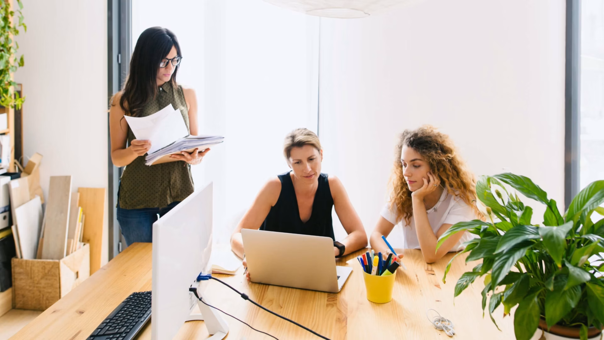 Three business people gather around a table with a laptop and paperwork, demonstrating what is a real estate broker