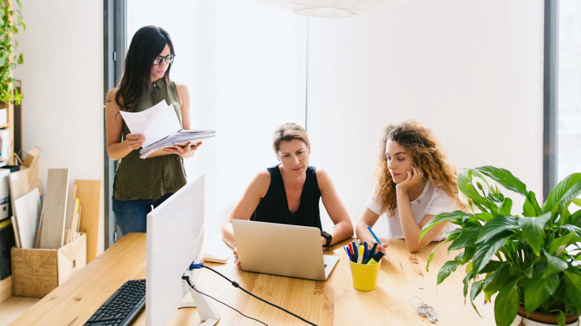 Three business people gather around a table with a laptop and paperwork, demonstrating what is a real estate broker