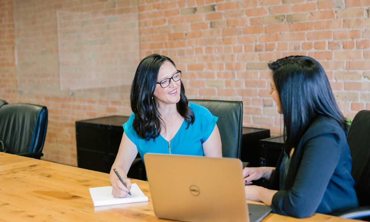 Real estate agent sitting at a large table with exposed brick walls behind her, going over her buyer agent commission models with a new homebuyer client