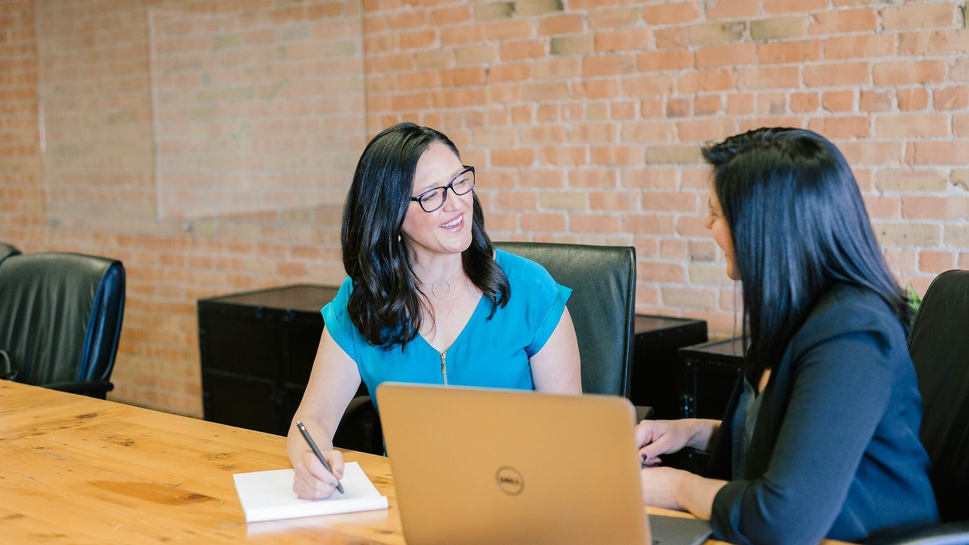 Real estate agent sitting at a large table with exposed brick walls behind her, going over her buyer agent commission models with a new homebuyer client