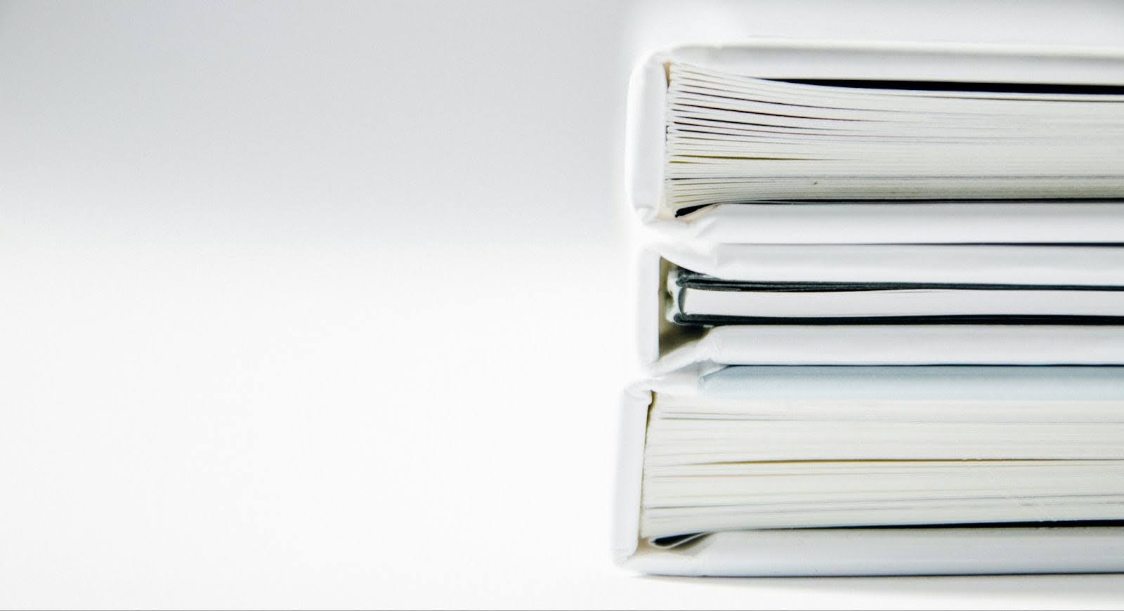 A stack of three white binders sits on a white background, representing some of the best books for real estate agents