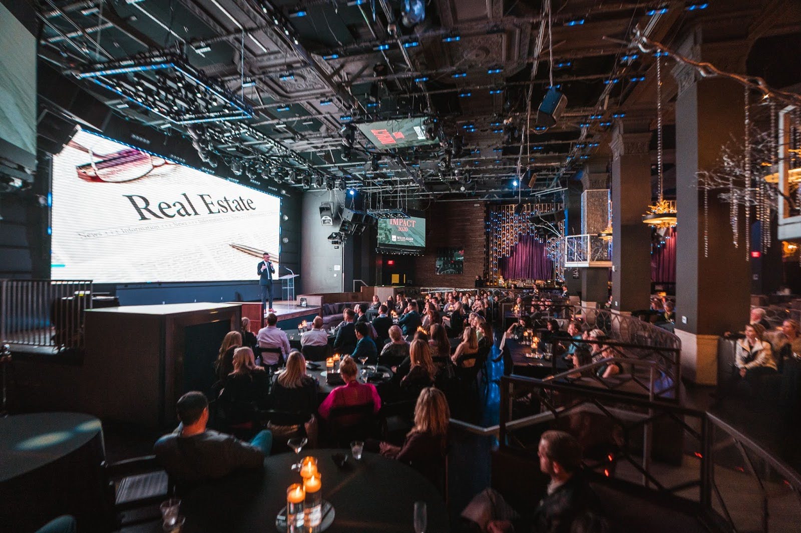 Audie Chamberlain stands on a stage in front of a large audience of real estate professionals explaining how to execute a PR campaign