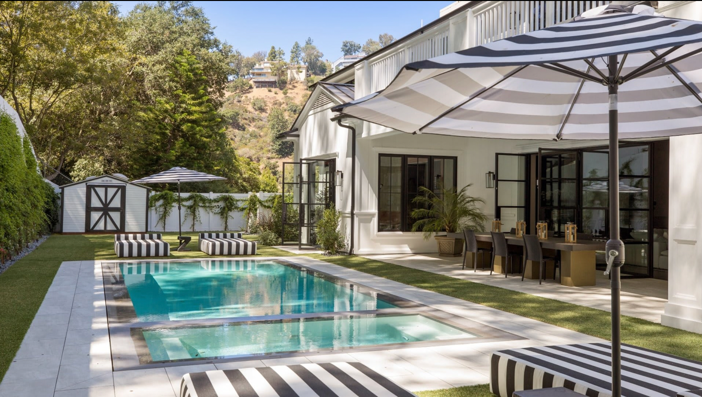 A teal in-ground pool with open sun umbrella in the foreground